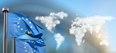 Imagen de banderas de la Unión Europea ondeando al viento y en el fondo, un mapa del mundo hecho con nubes, en pequeño
