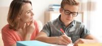 Una madre apoya en los estudios a su hijo que está con los libros sobre la mesa