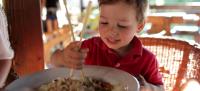 Niño intentando comer unos espaguetis con palillos