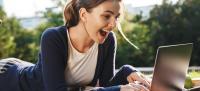 Chica alegre y sorprendida mirando un portátil en un parque